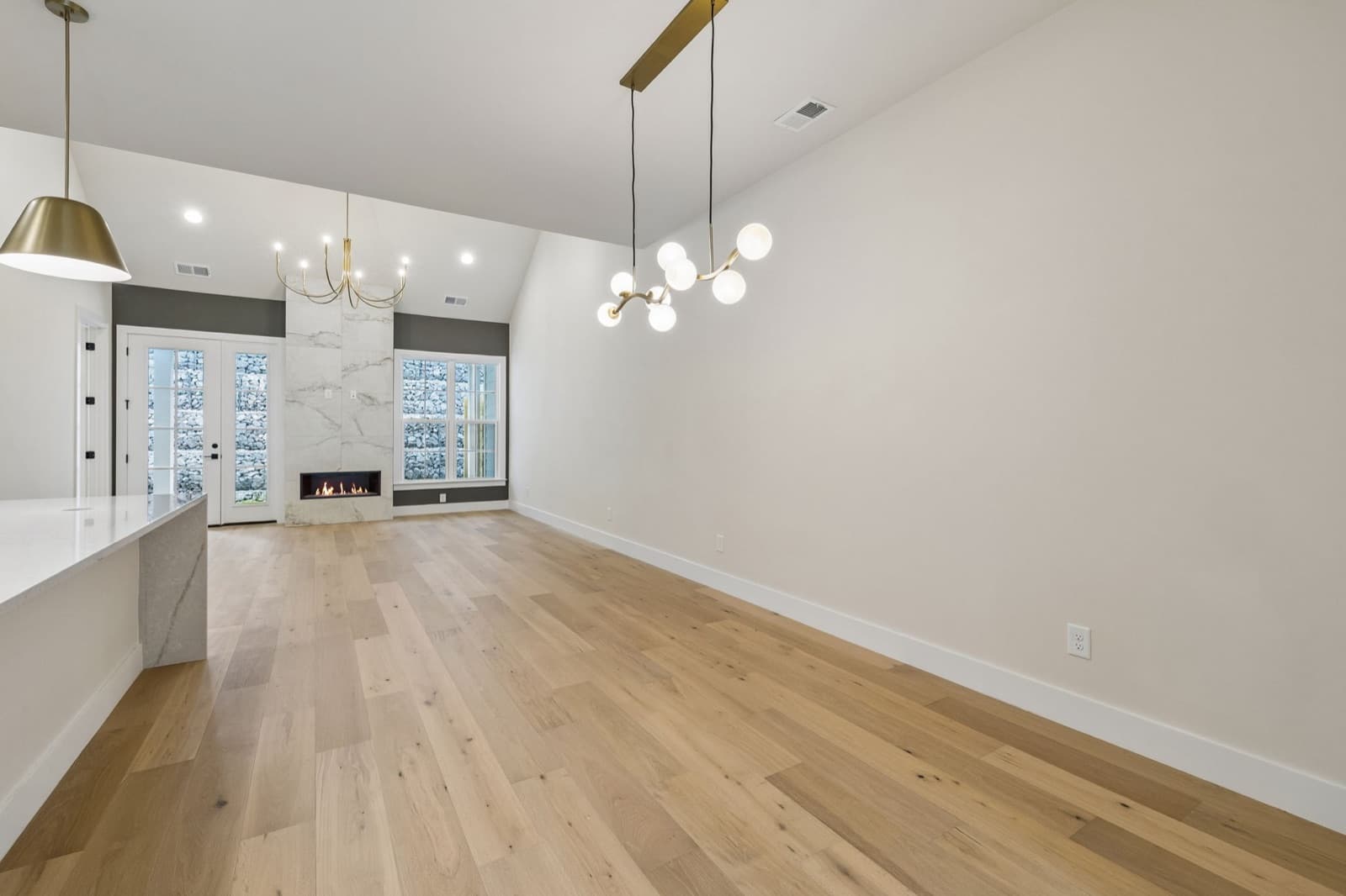 Open dining area at 123 under a brass globe chandelier, with the lit fireplace and French doors beyond.