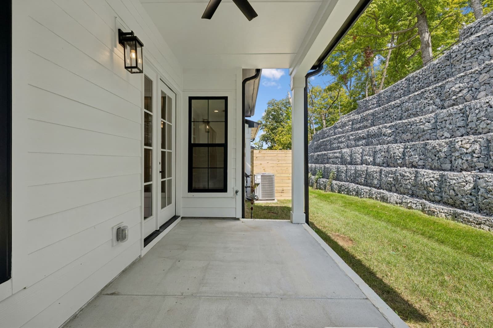 Covered patio at 123 Shadow Springs facing a tiered stacked-stone wall across a strip of lawn.