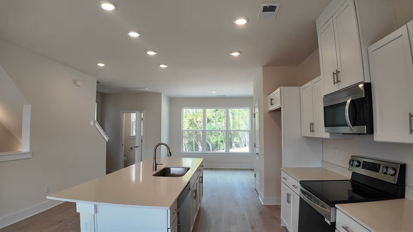 Kitchen at 2008 Sonya Terrace: a long white island with an undermount sink, white shaker cabinets, a stainless range and microwave with a tall cabinet above, recessed ceiling lights, and a triple window over the dining area at the far end.